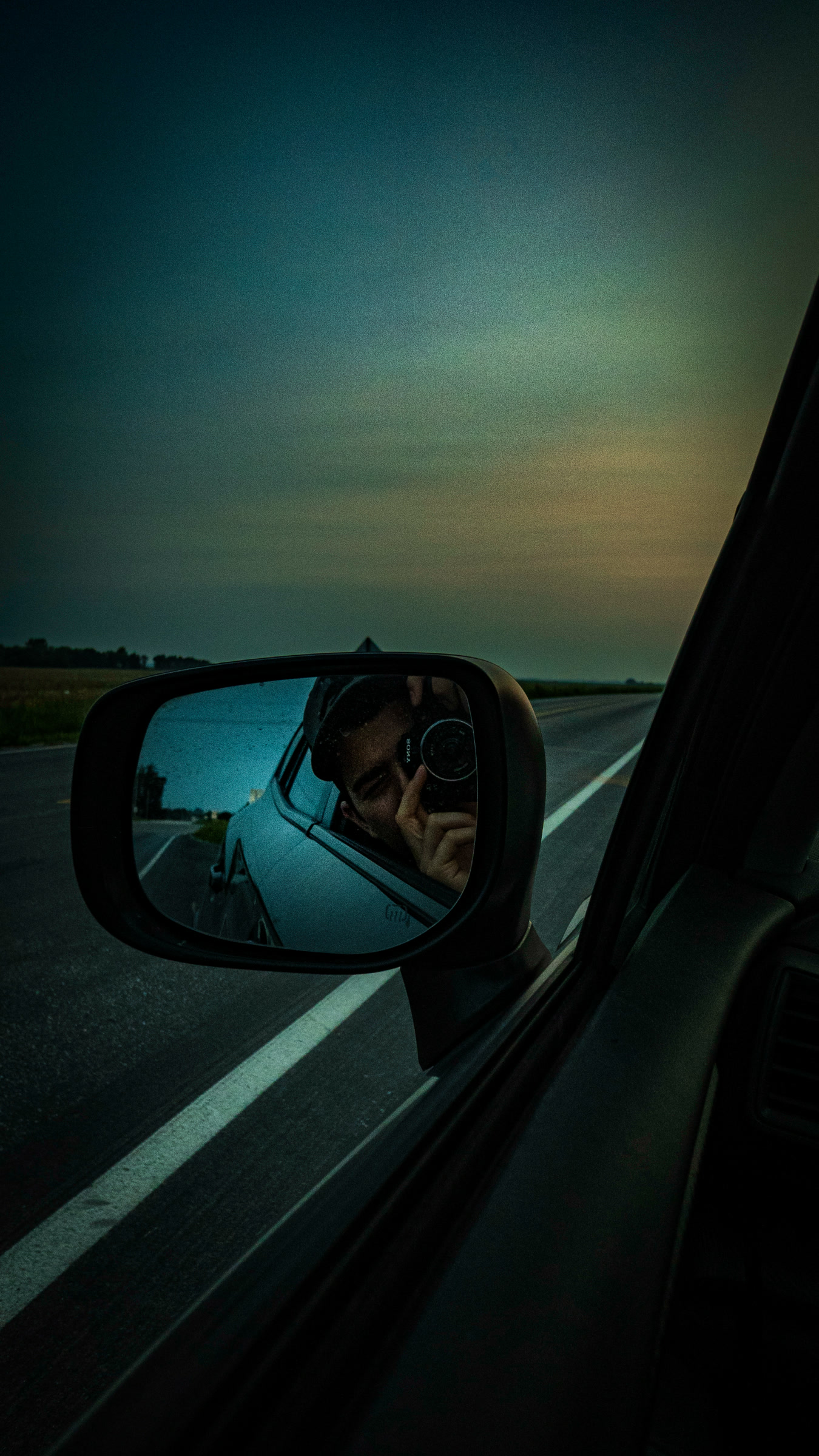 Matthew photographing his reflection with his camera in a car mirror